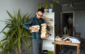 Imagem de um homem segurando vários livros nas mãos para organizá-los em uma estante.