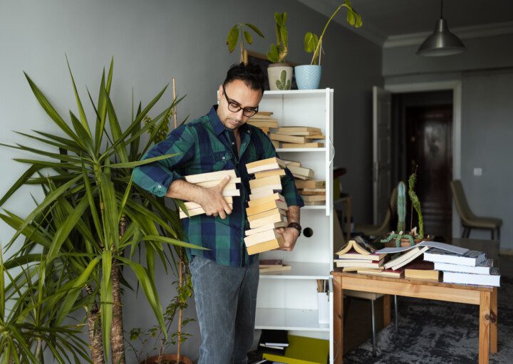 Imagem de um homem segurando vários livros nas mãos para organizá-los em uma estante.