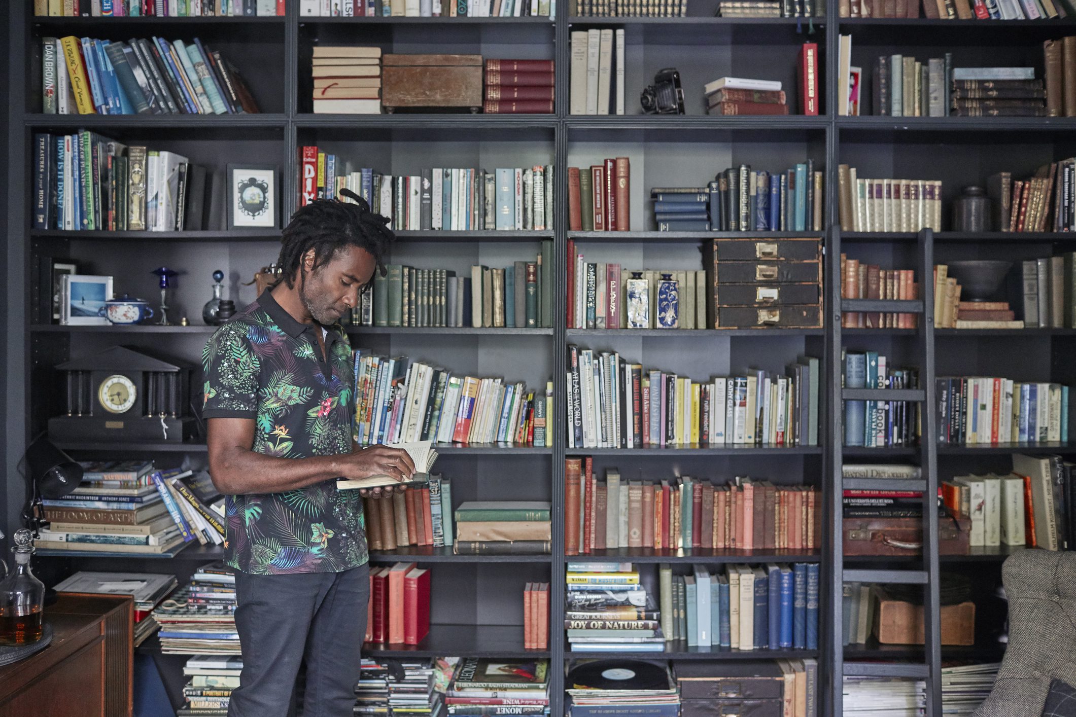 Imagem de um homem lendo um livro em frente a uma estante cheia de exemplares.