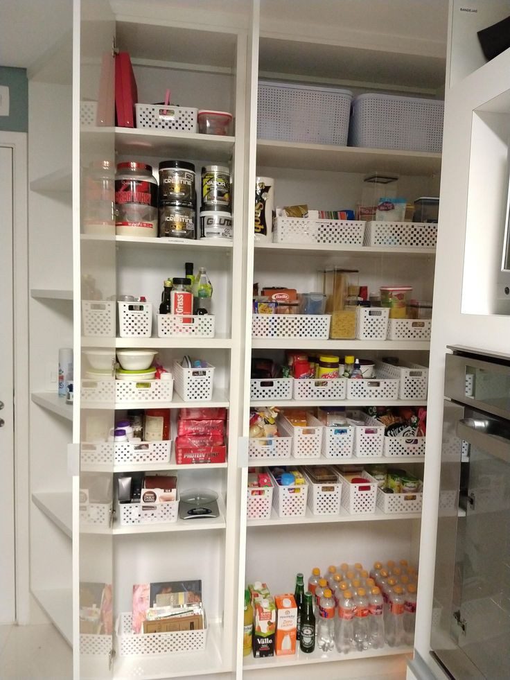 A foto mostra um exemplo de organizadores para a casa do modelo de cestos com alimentos que estão enfileirados em prateleiras de uma despensa.