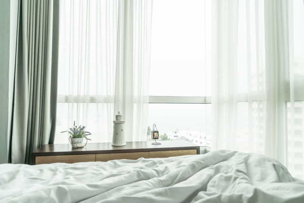 imagem que ilustra matéria sobre como escurecer quarto mostra quarto com iluminado com janela que tem cortinas de tecido