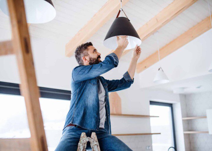 Em artigo sobre como emitir segunda via enel e trocar titularidade da conta, temos a imagem de um homem trocando a lâmpada de uma luminária de teto