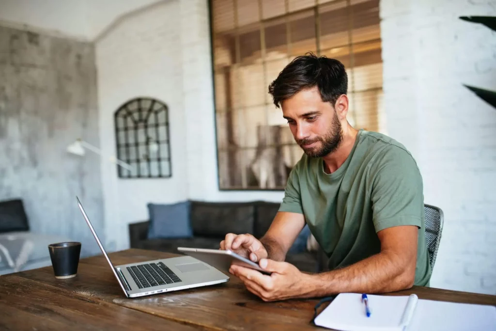 Imagem de um homem fazendo contas em um tablet enquanto está sentado em frente a uma mesa com alguns papéis, um notebook e uma caneca de café em um imóvel para ilustrar matéria sobre planejamento financeiro