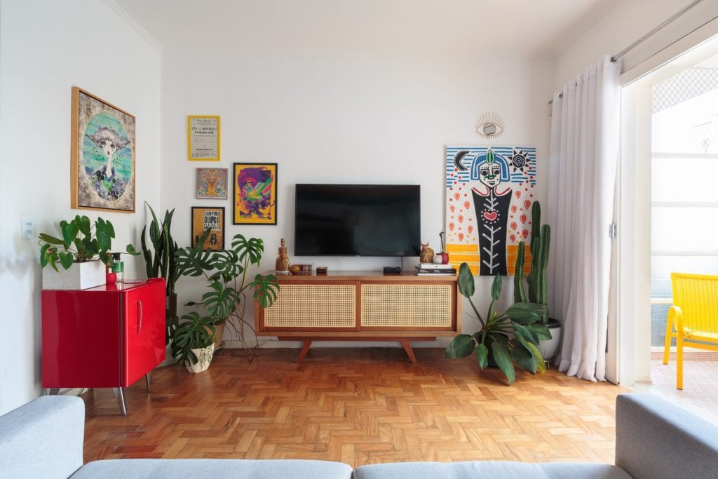 Sala de apartamento na Avenida Paulista, com quadros na parede, plantas e móveis aparadores.