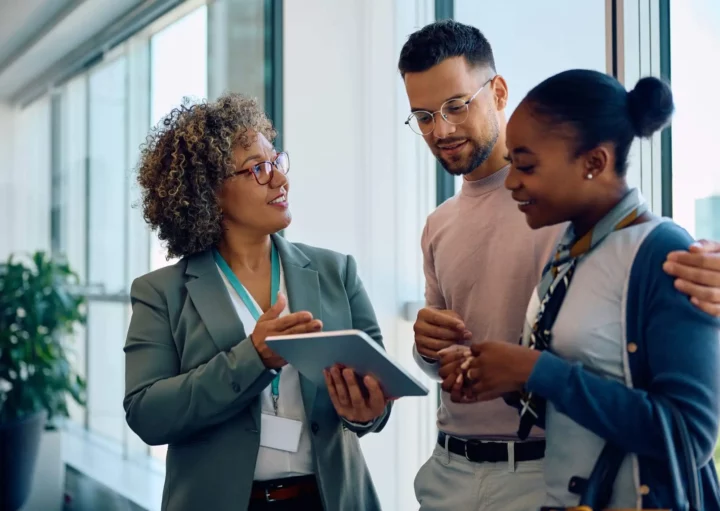 Imagem de um casal formado por um homem e uma mulher recebendo informações de uma corretora de imóveis em uma reunião para ilustrar matéria sobre corretagem de imóveis
