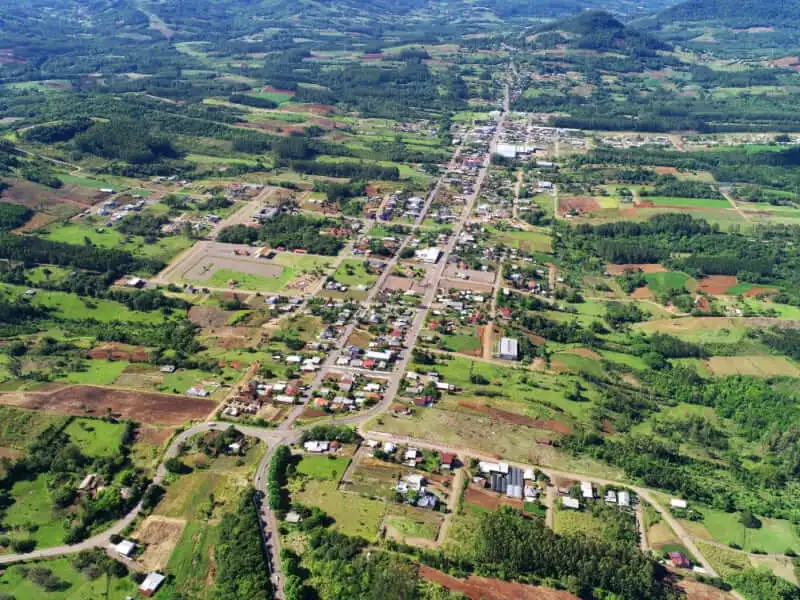 Imagem da vista aérea de Presidente Lucena, no Rio Grande do Sul, mostra uma estrada principal passando pelo centro, cercada por campos verdes e fazendas