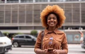 Imagem de uma mulher parada em frente a um prédio na cidade de São Paulo sorrindo para ilustrar matéria sobre os melhores bairros para morar em SP