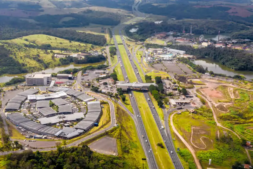 Imagem da vista aérea de uma rodovia em Itupeva, em São Paulo, cercada por áreas verdes, prédios comerciais, estacionamentos e um rio visível ao fundo