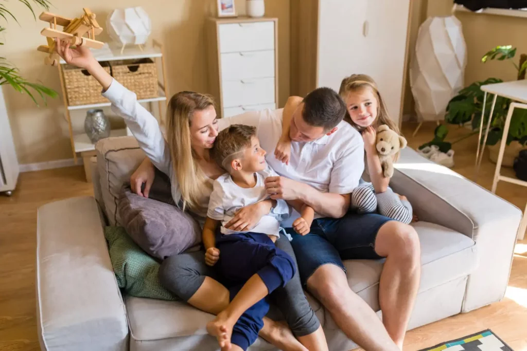 Imagem de uma família composta por um homem, uma mulher e duas crianças brincando no sofá que está na sala de uma casa para ilustrar matéria sobre as melhores cidades do Brasil para morar