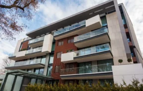 Imagem tirada de baixo para cima de um prédio moderno em um dia de céu azul para ilustrar matéria sobre como comprar um apartamento