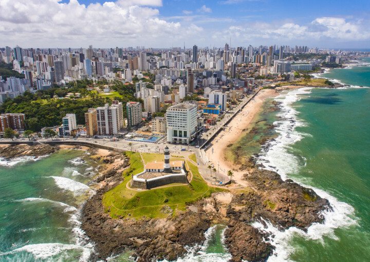 Foto que ilustra matéria sobre os melhores bairros de Salvador mostra os prédios do bairro da Barra vistos do alto, com o Farol da Barra e pedaços da praia em primeiro plano.