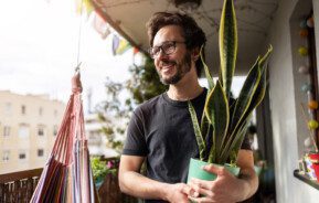 Em foto que ilustra um teste de personalidades sobre plantas em casa, um homem segura um vaso com uma planta da espécie espada de São Jorge.