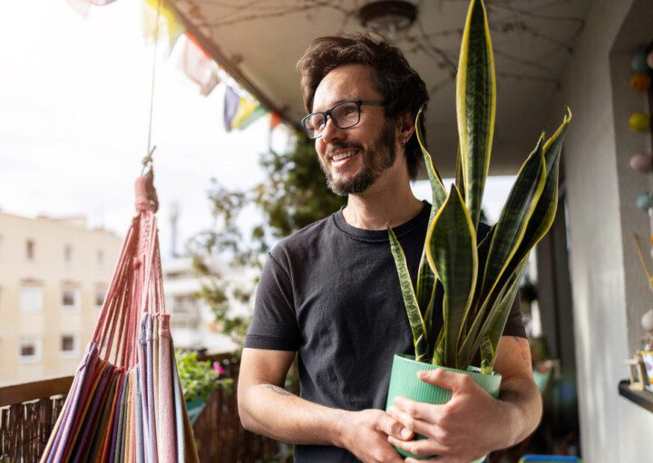 Em foto que ilustra um teste de personalidades sobre plantas em casa, um homem segura um vaso com uma planta da espécie espada de São Jorge.