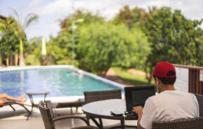 Homem usando computador sentado diante de uma piscina