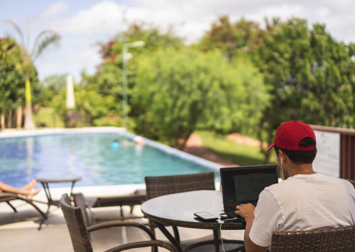 Homem usando computador sentado diante de uma piscina