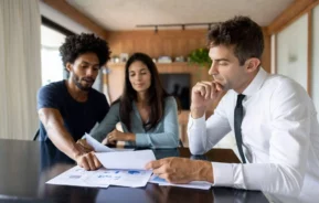 Imagem de um casal formado por um homem e uma mulher conversando com um profissional especializado no ramo imobiliário para ilustrar matéria sobre inventário de imóvel