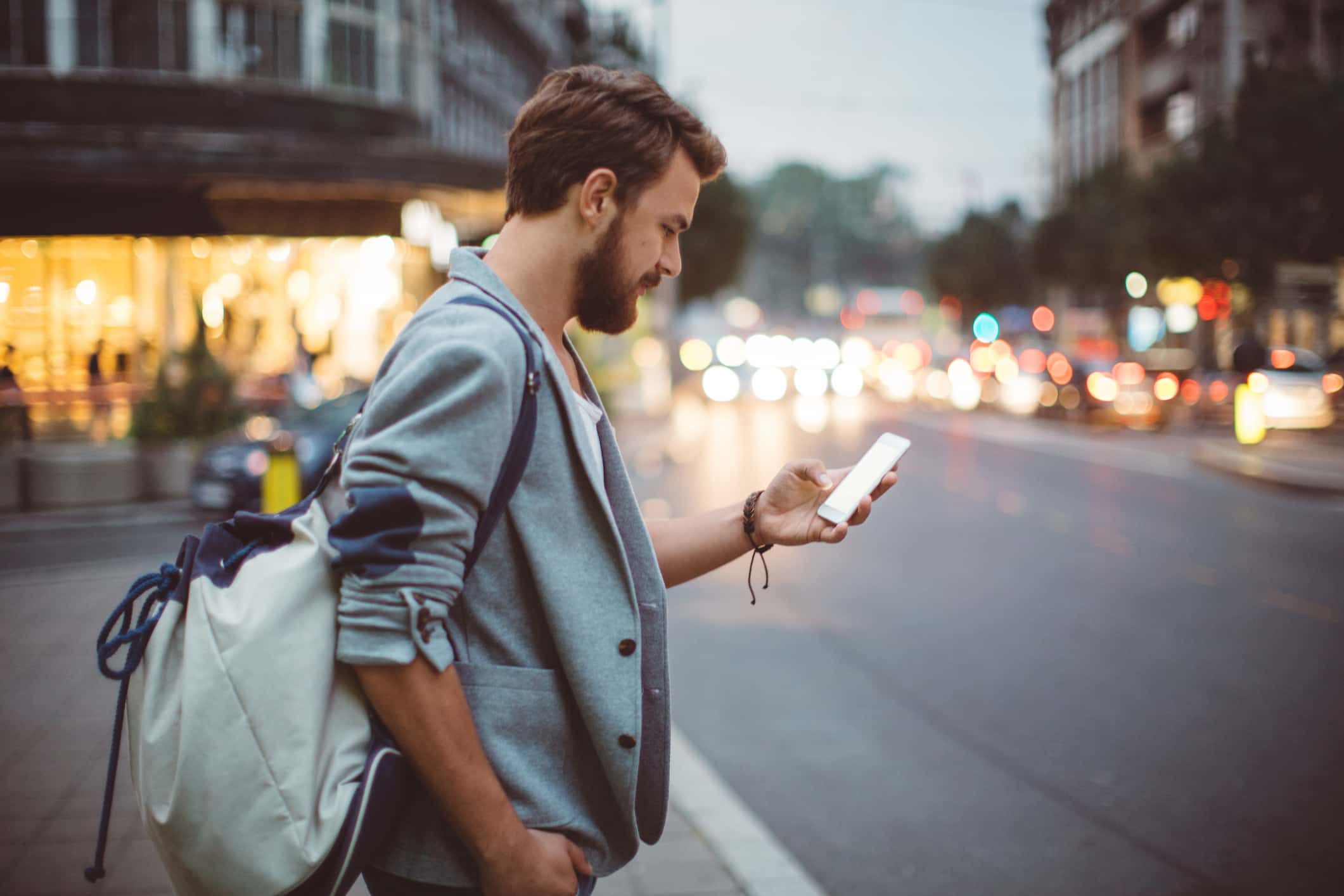 Homem com mochila, na rua, usando o celular enquanto pensa em mudar de cidade.