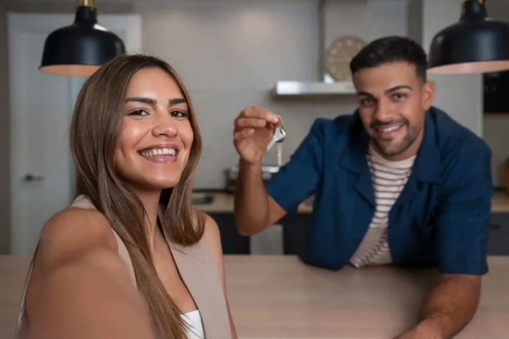 Imagem de um casal formado por um homem e uma mulher sorrindo para uma foto com a chave de um imóvel na mão dentro da cozinha de uma casa para ilustrar matéria sobre os tipos de usufruto