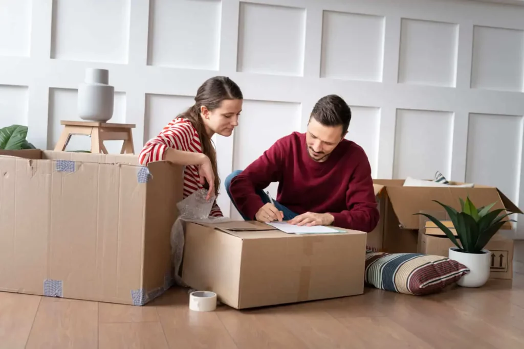 Imagem de um casal formado por um homem e uma mulher sentados no chão de uma casa entre caixas de papelão fechadas para ilustrar matéria sobre a cidade com menor custo de vida no Brasil