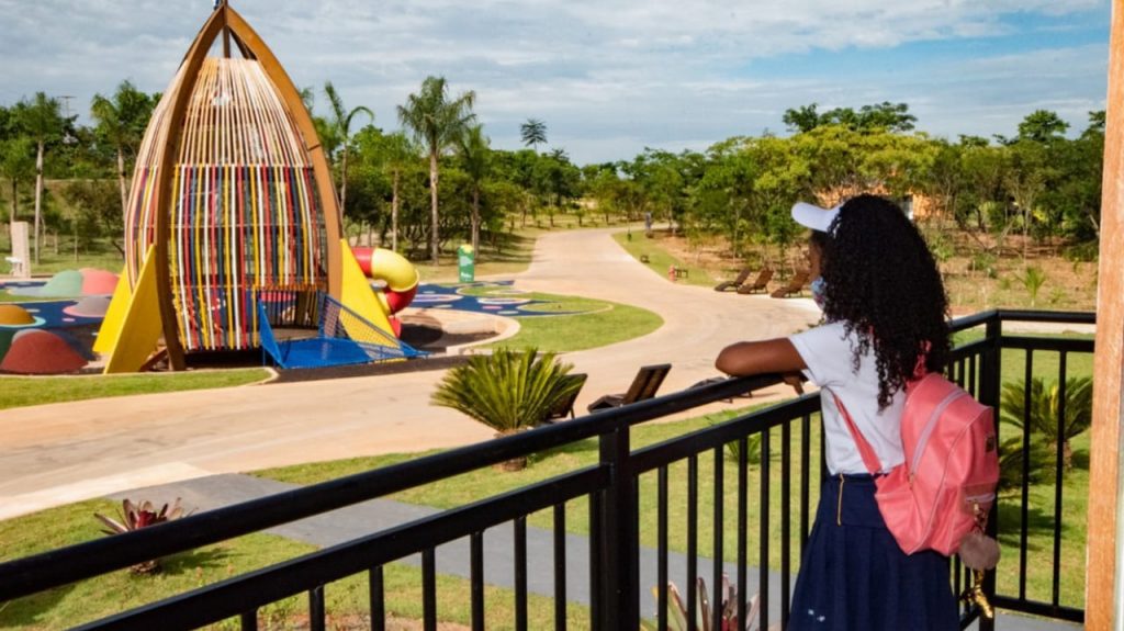 criança, de máscara, olha para área conhecida como mundo das crianças, no parque da cidade. No centro, brinquedo colorido em formato de foguete