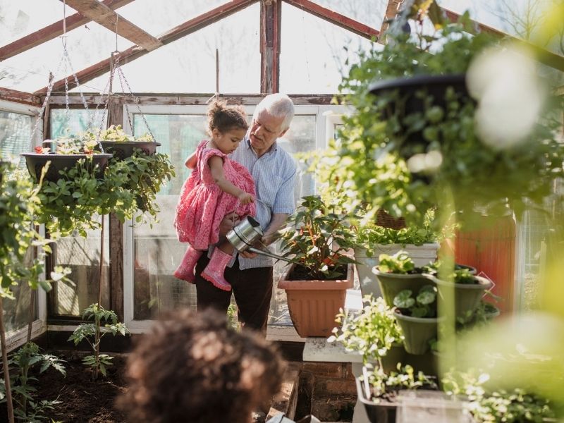 homem mais velho com uma criança no colo olhando os arredores de um jardim com teto solar e paredes de material transparente