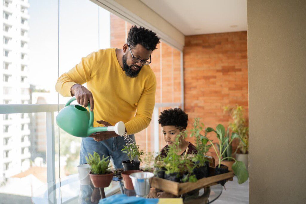 Pai e filho regando a horta em um apartamento.