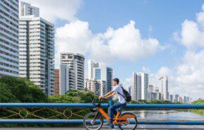 homem andando de bicicleta às margens de um rio, com prédios na lateral esquerda da foto em Recife