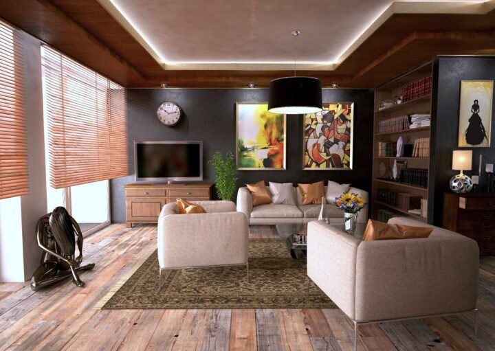 Foto que ilustra matéria sobre objetos de decoração para sala mostra uma sala com um jogo de poltronas brancas dispostas de frente para um sofá, ao fundo e mais à direita, com o mesmo tecido. Atrás do sofá, dois quadros coloridos na parede. Nessa mesma parede, ao fundo e à esquerda, há um rack com uma TV.