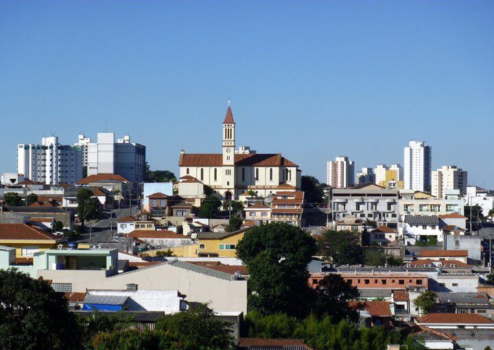 Foto que ilustra matéria sobre a Zona Leste de SP mostra uma panorâmica do bairro de Vila Matilde, com uma igreja ao fundo, no centro da tela, e um céu azul.