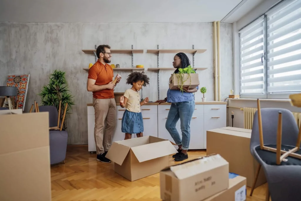 Imagem de uma família formada por um homem, uma mulher e uma criança tirando a mudança de caixas de papelão que estão espalhadas por um imóvel para ilustrar matéria sobre apartamento para alugar na Zona Norte de SP