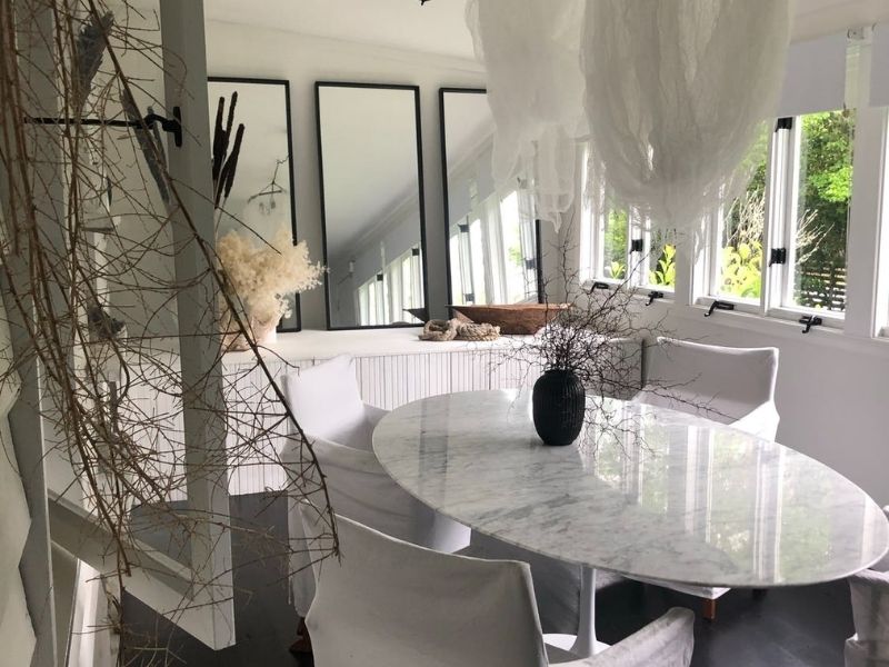 Sala de jantar estilo contemporâneo, com mesa branca e cadeiras brancas e três espelhos na parede ao fundo