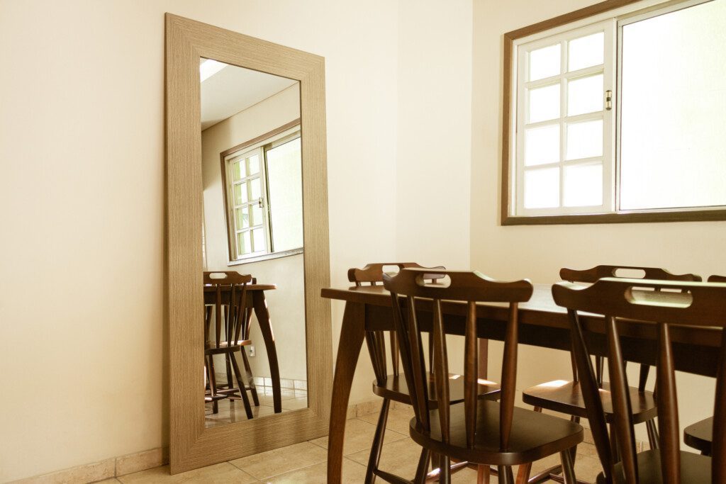 Sala de jantar com espelho simples no chão e conjunto de mesa e cadeiras em madeira maciça.