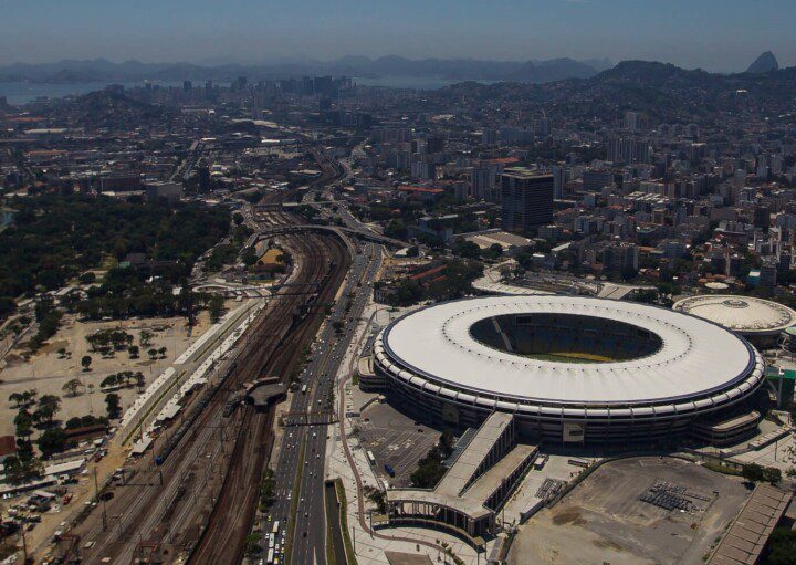 Foto que ilustra matéria sobre a Zona Norte do RJ mostra uma visão do alto do Maracanã, que aparece mais à direita da tela, com a linha do trem à esquerda e, ao fundo, o resto da cidade, com toda a região Central, a Baía de Guanabara e as montanhas ao fundo.