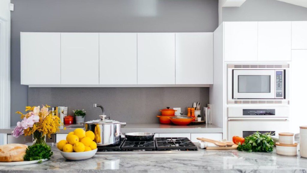 Cozinha com um balcão de mármore. Acima, frutas e itens decorativos. Na parede, armários e um microondas.