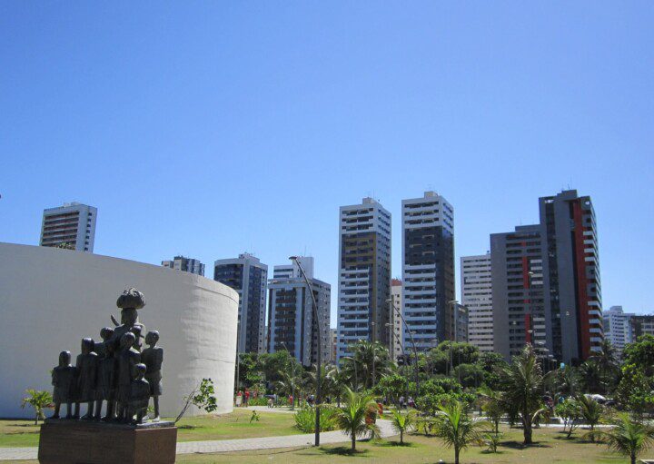 Foto que ilustra matéria sobre parques em Recife mostra uma panorâmica do Parque Dona Lindu, com uma escultura em primeiro plano, mais à esquerda, árvores à direita e grandes prédios residenciais ao fundo.