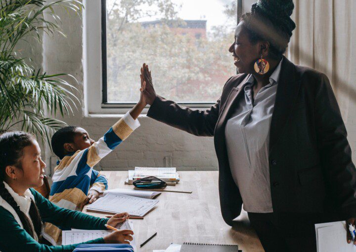 Foto que ilustra matéria sobre melhores escolas em Recife mostra uma professora negra fazendo um gesto de toca aí com um aluno, enquanto uma aluna ao lado observa