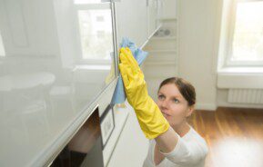 Mulher com uma camiseta branca limpando o armário da cozinha com produtos caseiros que acabam com formigas.