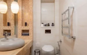 Imagem de um lavabo moderno com uma vaso sanitário super estiloso, parede com porcelanatos em tons de creme, uma pia moderna em formato circular com uma pedra cinza e uma luminária.