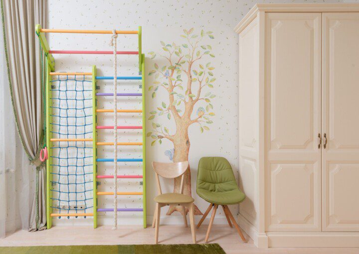 Decoração de quarto infantil em tons claros e verdes, adesivos de parede com uma árvore e folhas decorativas, além de móveis em cor bege.