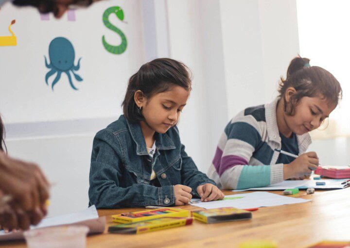 Foto que ilustra matéria sobre escolas em São Caetano do Sul mostra duas meninas, sentadas lado a lado à uma mesa enquanto fazem desenhos em folhas de papel.