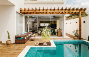 área externa de uma casa com piscina em deck de madeira, sofás e plantas em volta