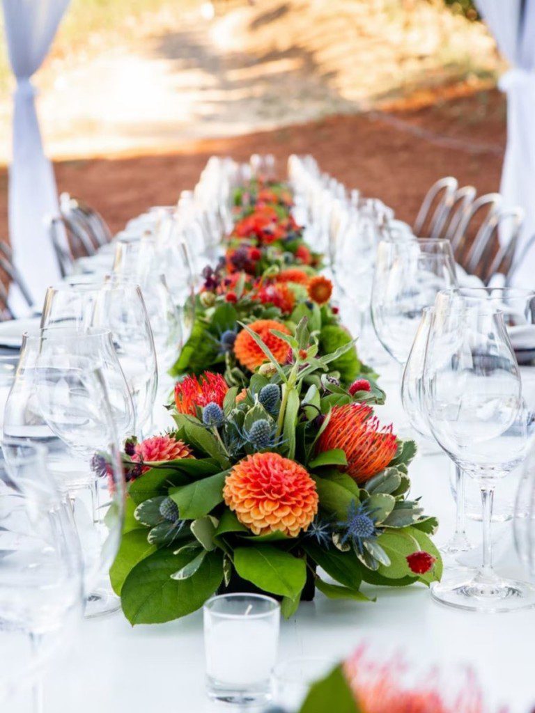 mesa posta com copos e taças de vidro e arranjo central nas cores primárias