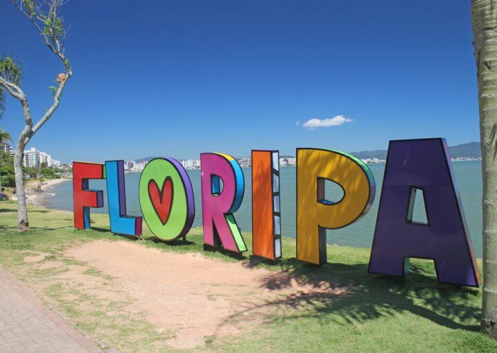 Foto que ilustra matéria sobre o que fazer em Florianópolis mostra em detalhes um letreiro com a palavra “Floripa” escrita em letras coloridas à beira de uma das praias da cidade.