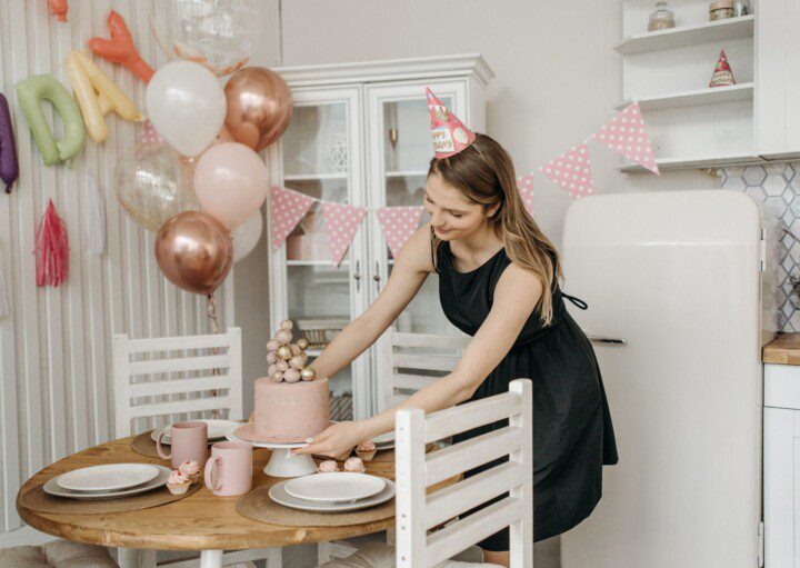 Imagem de uma moça arrumando o bolo com uma decoração de festa simples com balões em tons de rosa e rose gold.