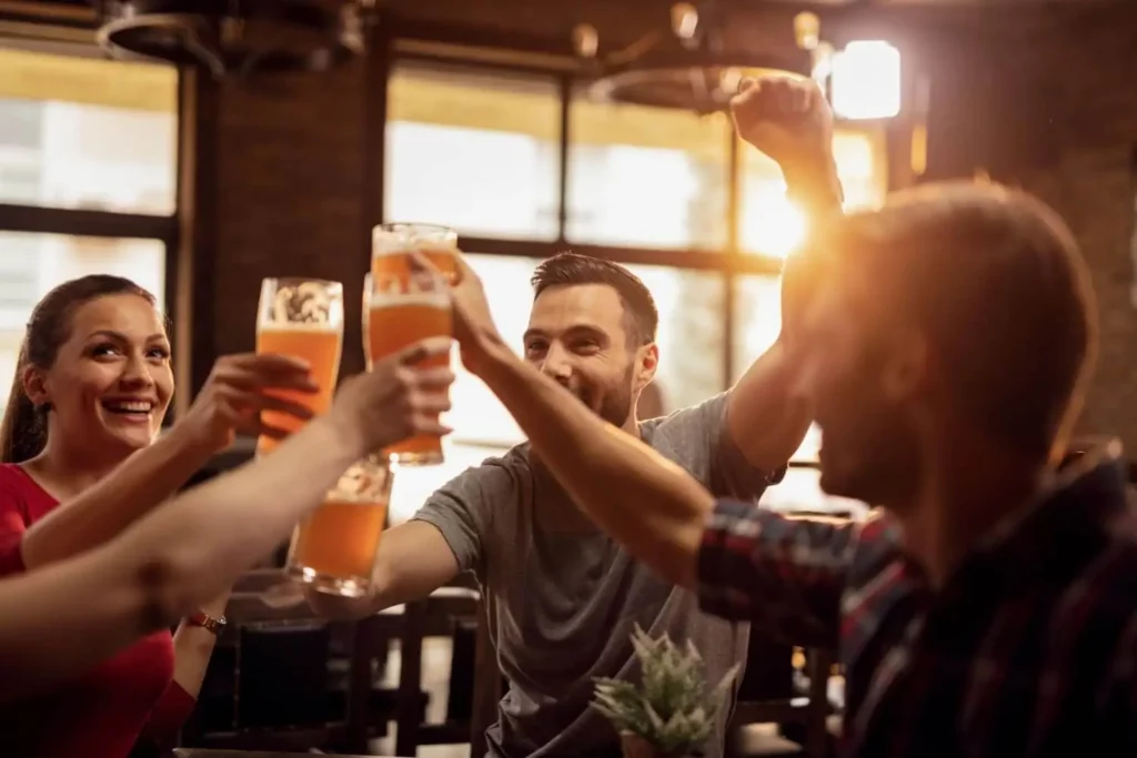 Imagem de amigos em um bar brindando com copos de cerveja para ilustrar matéria sobre quais são os bairros da Zona Oeste de SP