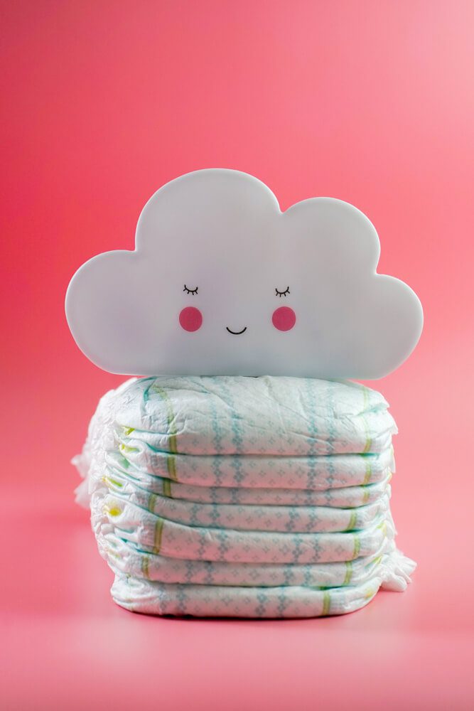 A imagem mostra várias fraldas, uma em cima da outra. Em cima delas há o desenho de uma nuvem sorrindo.