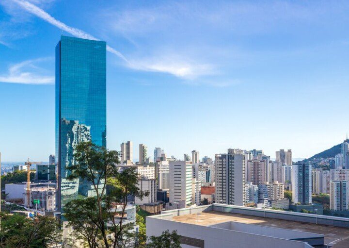 Foto que ilustra matéria sobre as melhores cidades de Minas Gerais mostra uma panorâmica de prédios da cidade de Nova Lima, com destaque para um grande edifício, mais alto, totalmente espelhado