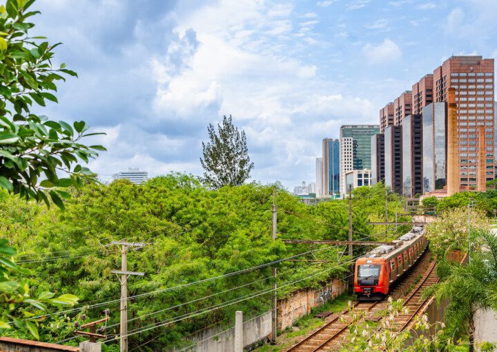 Foto que ilustra matéria sobre mapa trem sp mostra uma linha ferroviária com um trem em movimento com grama e árvores verdes dos lados