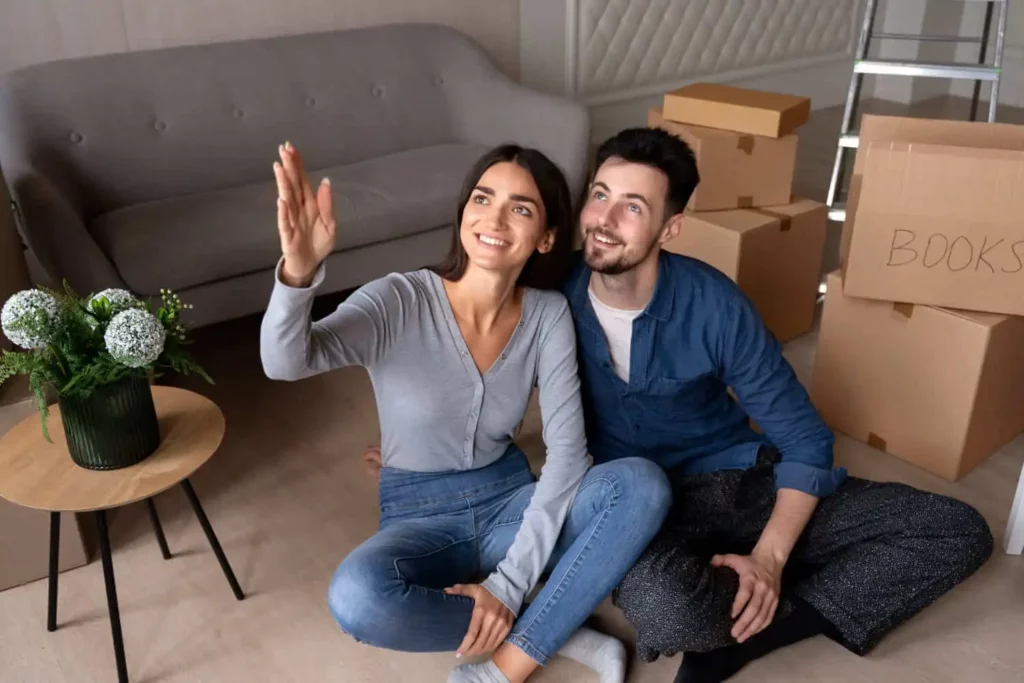 Imagem de um homem e uma mulher sentados na sala de um imóvel ao lado de um sofá, uma mesinha de centro e caixas de papelão para ilustrar matéria sobre como calcular devolução de caução de aluguel