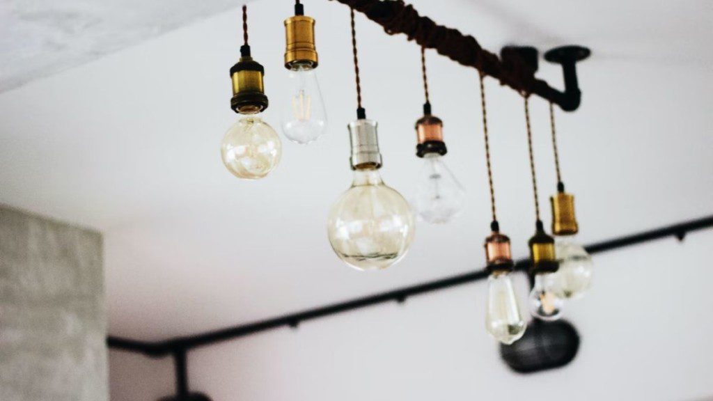 A imagem mostra luzes penduradas em iluminação no estilo de decoração industrial. As luzes são expostas e penduradas por uma tubulação aparente.